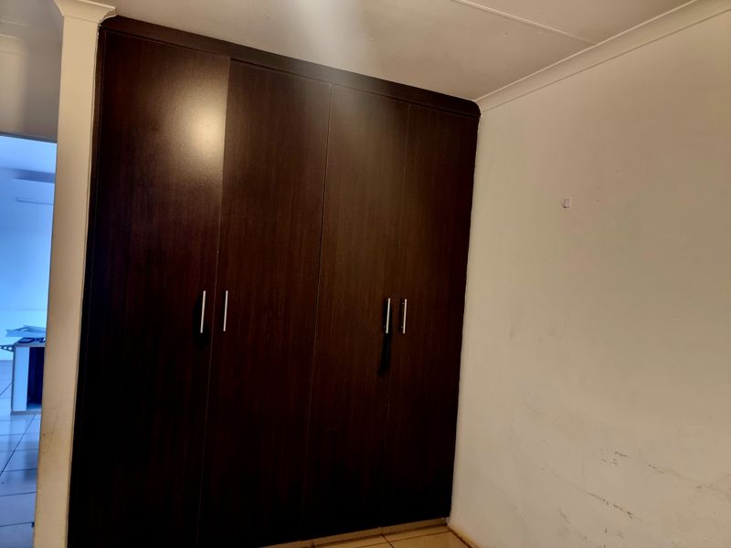 A bedroom featuring a dark wood-finish built-in wardrobe with modern handles and standard ceiling cornicing.