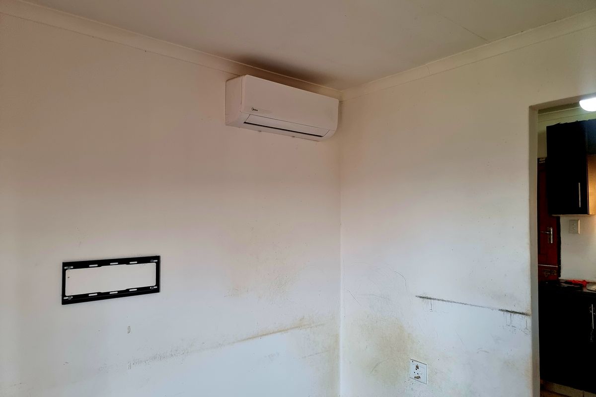 An empty living room area featuring a wall-mounted air conditioning unit and television bracket, showing signs of wear and requiring cosmetic wall repairs.