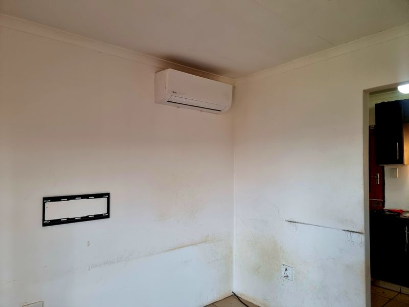 An empty living room area featuring a wall-mounted air conditioning unit and television bracket, showing signs of wear and requiring cosmetic wall repairs.