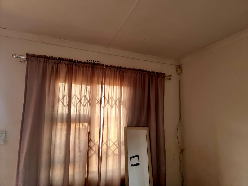 A bedroom interior featuring a window with a security gate, curtain rod, and wall-mounted alarm sensor.