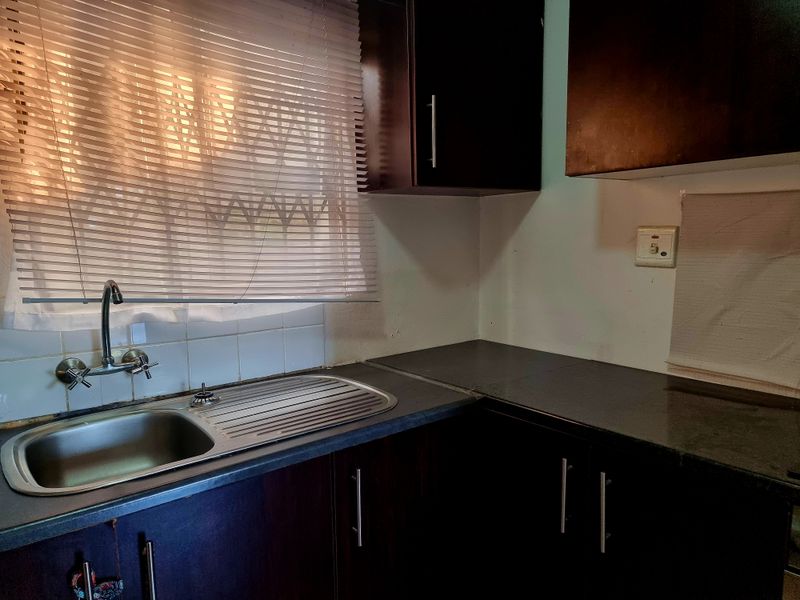 A functional kitchen area featuring dark wood cabinetry, laminate countertops, and a stainless steel sink with a tiled splashback.