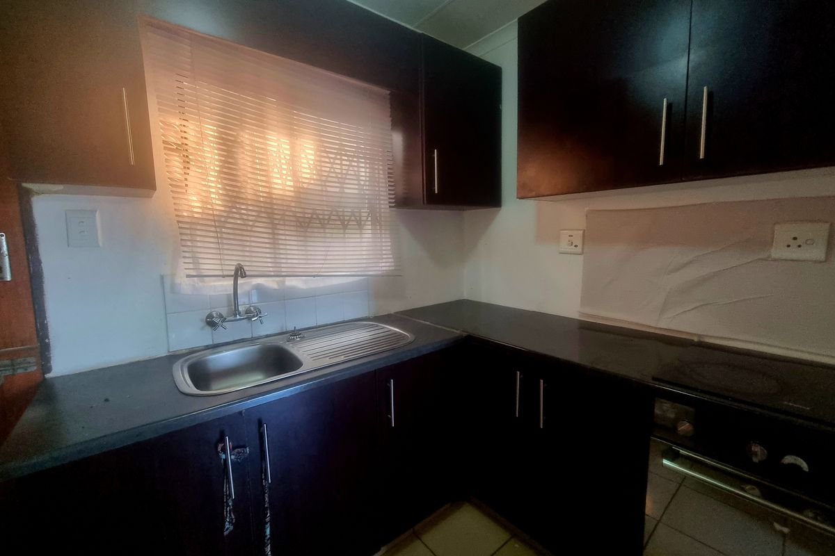 A functional kitchen featuring dark wood cabinetry, laminate countertops, a stainless steel sink, and a built-in oven with tiled flooring.