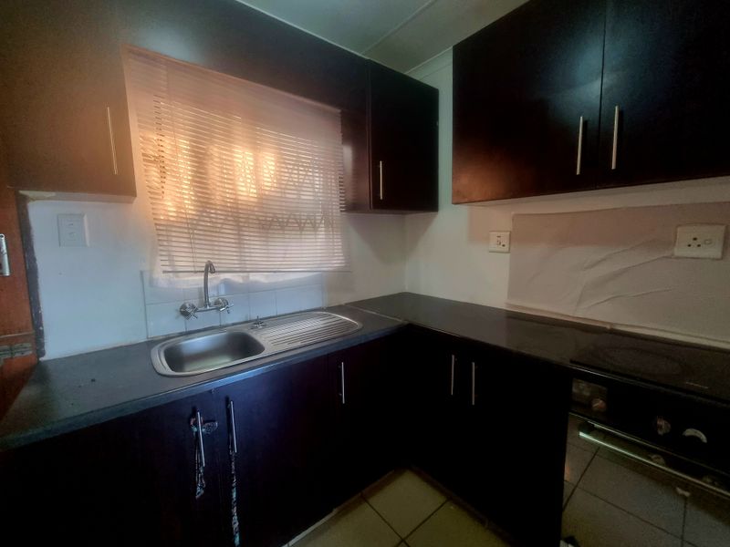 A functional kitchen featuring dark wood cabinetry, laminate countertops, a stainless steel sink, and a built-in oven with tiled flooring.