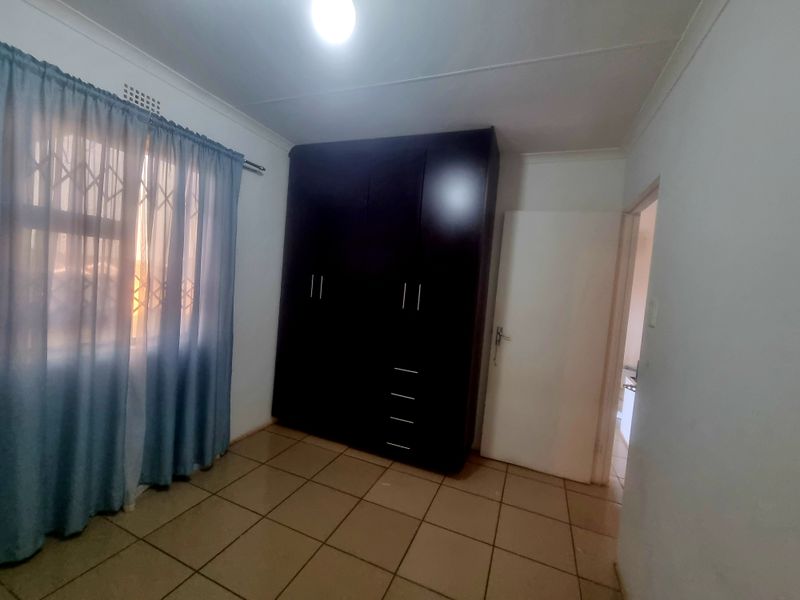A clean, empty bedroom featuring tiled flooring and dark built-in cupboards, offering a neutral space ready for personalization.