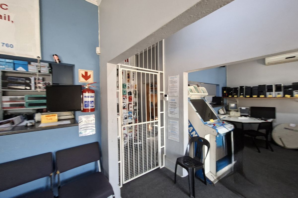 A functional utility or office space featuring a security gate, built-in shelving, and an air conditioning unit, currently utilized for commercial or technical purposes.