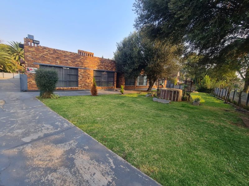 Rear view of a face brick house featuring a large lawn, mature trees, and a concrete driveway.