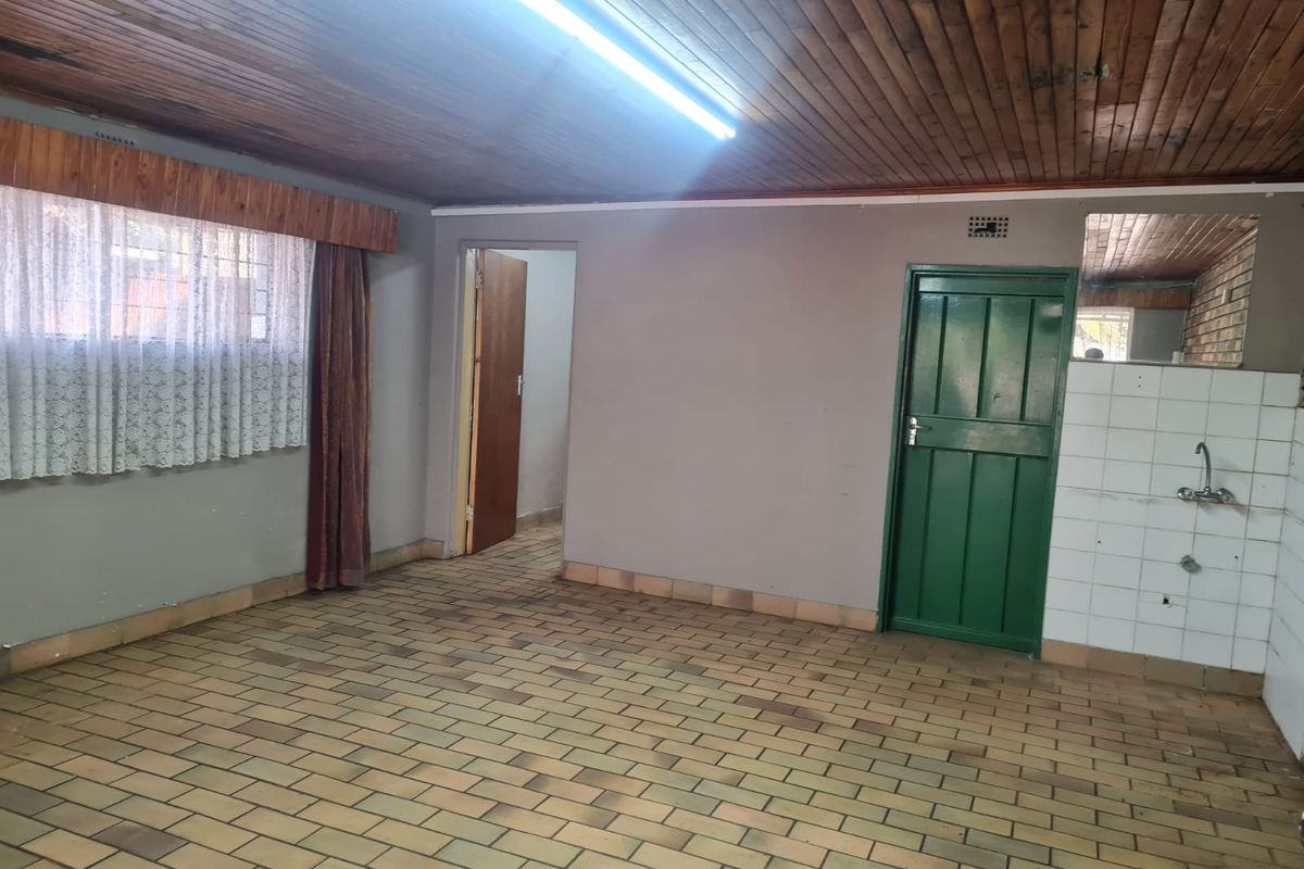 An empty kitchen area featuring brick-style floor tiles, a timber-clad ceiling, and basic plumbing fixtures, offering a blank canvas for renovation.