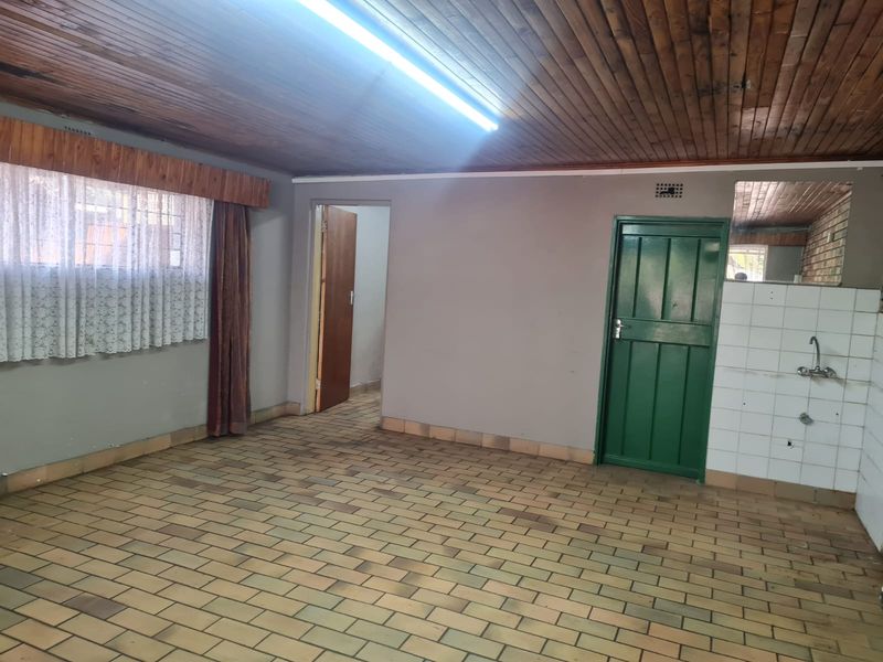 An empty kitchen area featuring brick-style floor tiles, a timber-clad ceiling, and basic plumbing fixtures, offering a blank canvas for renovation.