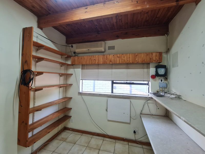 A functional office space featuring timber ceilings, built-in shelving, a desk, and a split-system air conditioner, requiring cosmetic updates to improve its overall condition.