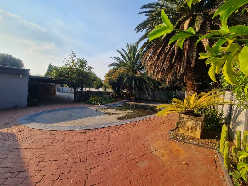 Outdoor pool area featuring a swimming pool with a cover, surrounded by brick paving and established garden landscaping.