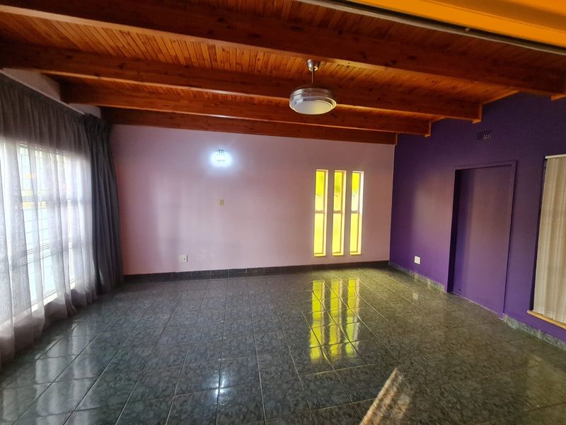 An empty living room featuring exposed timber beam ceilings, tiled flooring, and unique vertical slit windows, offering a blank canvas for interior design.