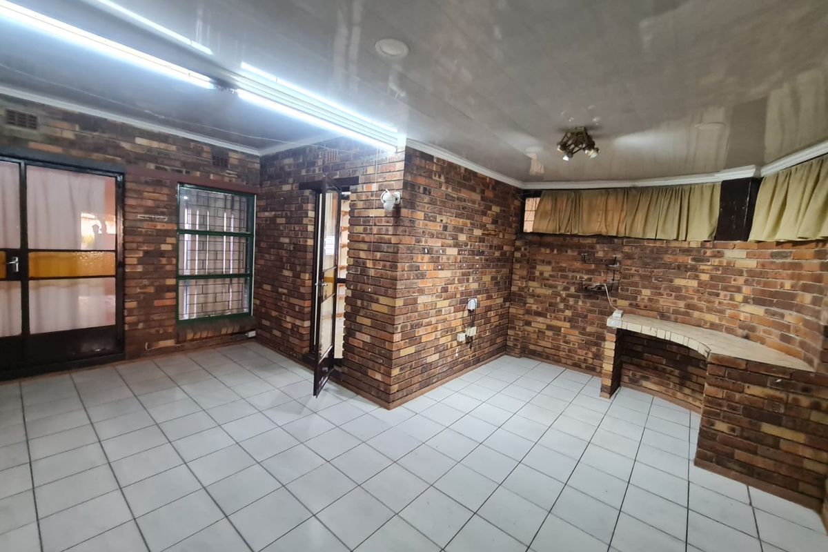 An empty living area featuring exposed brick walls, tiled flooring, and a built-in brick counter, offering a rustic aesthetic with potential for modernization.