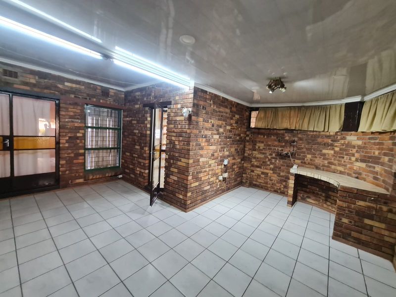 An empty living area featuring exposed brick walls, tiled flooring, and a built-in brick counter, offering a rustic aesthetic with potential for modernization.