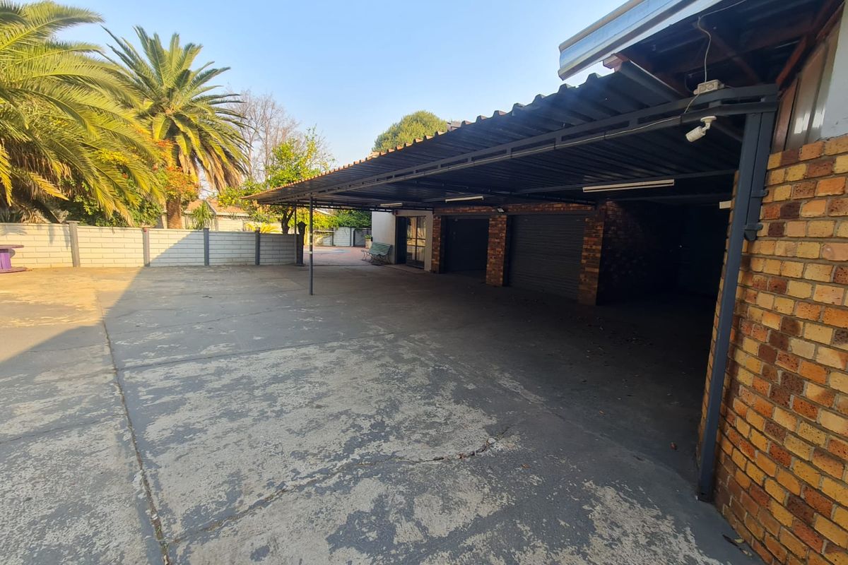 A spacious outdoor carport area featuring a corrugated metal roof, brick support pillars, and a large concrete driveway.