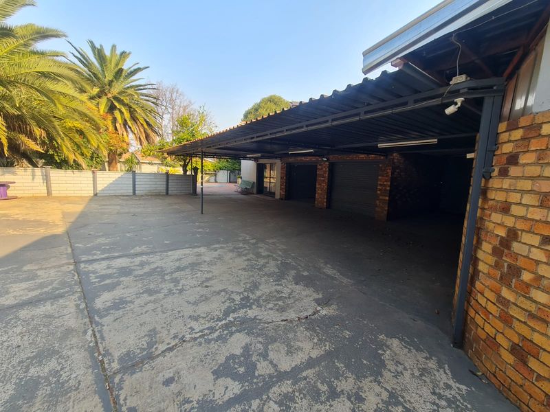 A spacious outdoor carport area featuring a corrugated metal roof, brick support pillars, and a large concrete driveway.