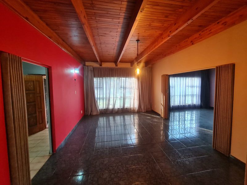 Spacious living area featuring a high exposed timber beam ceiling, tiled flooring, and a folding room divider, offering a versatile open-plan layout.