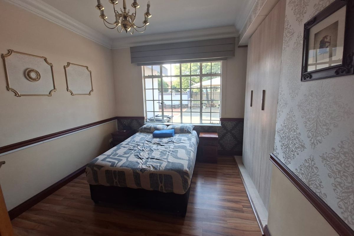 A well-maintained bedroom featuring laminate flooring, built-in cupboards, decorative dado rails, and a classic chandelier, offering a comfortable and functional living space.