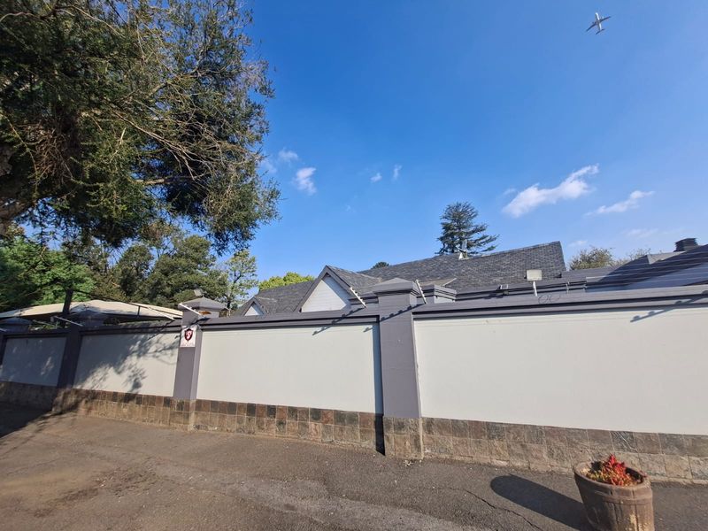 A view of the property's front perimeter wall featuring stone cladding, secure electric fencing, and a tiled roof visible in the background.