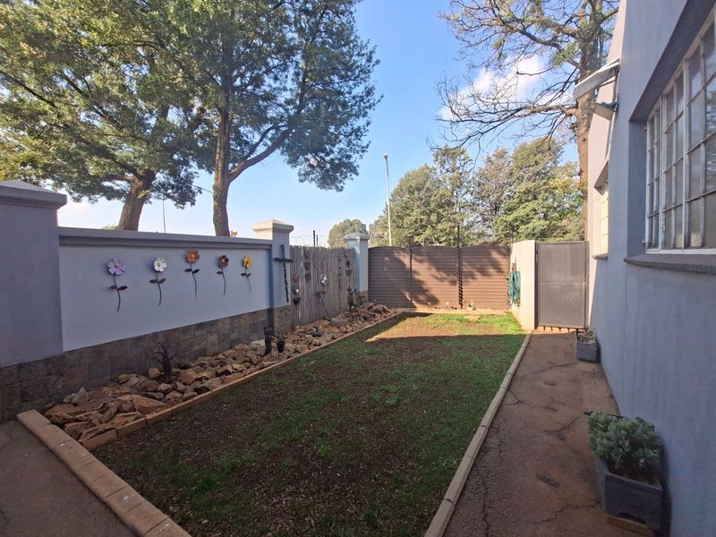 A private rear garden area featuring a paved walkway, stone-clad boundary wall, and secure metal gate access.