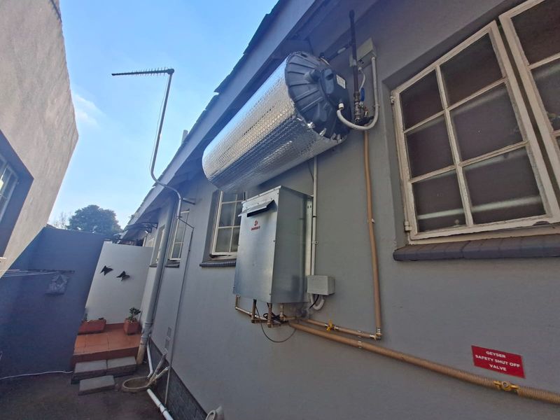 Exterior view of the property showing a wall-mounted geyser and gas water heater unit with associated plumbing and an external television antenna.