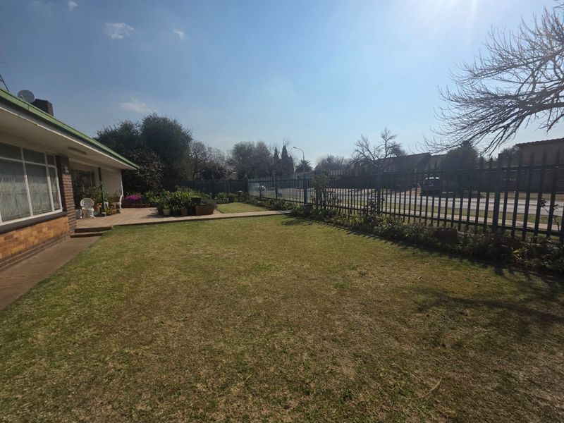 Front yard view featuring a paved patio area, established lawn, and secure metal perimeter fencing along the street boundary.