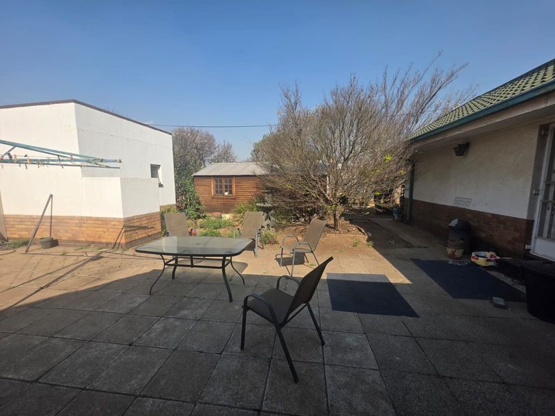 A rear exterior view featuring a paved patio area, a timber garden shed, and access to the main dwelling structure.