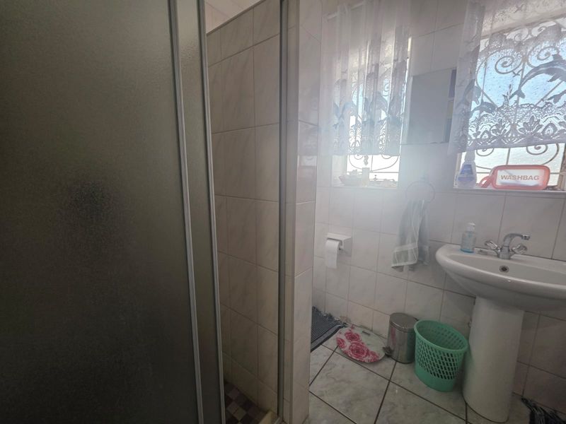 A functional bathroom featuring a pedestal basin, tiled walls and flooring, and a separate shower enclosure with a glass door.