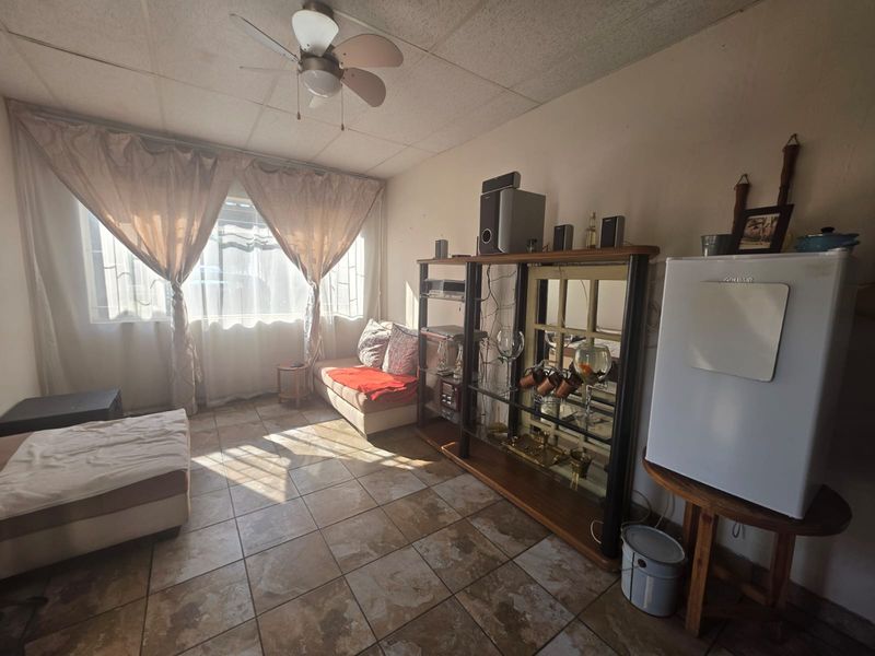 A living room featuring tiled flooring, a ceiling fan, and natural light through a window with security bars.