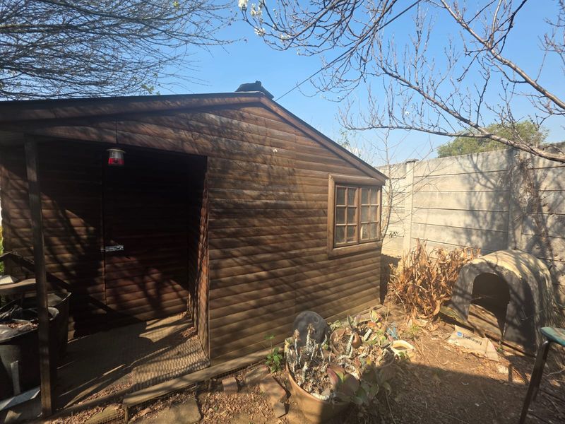 A detached timber utility shed located in the rear garden area, featuring wood cladding and a small window.