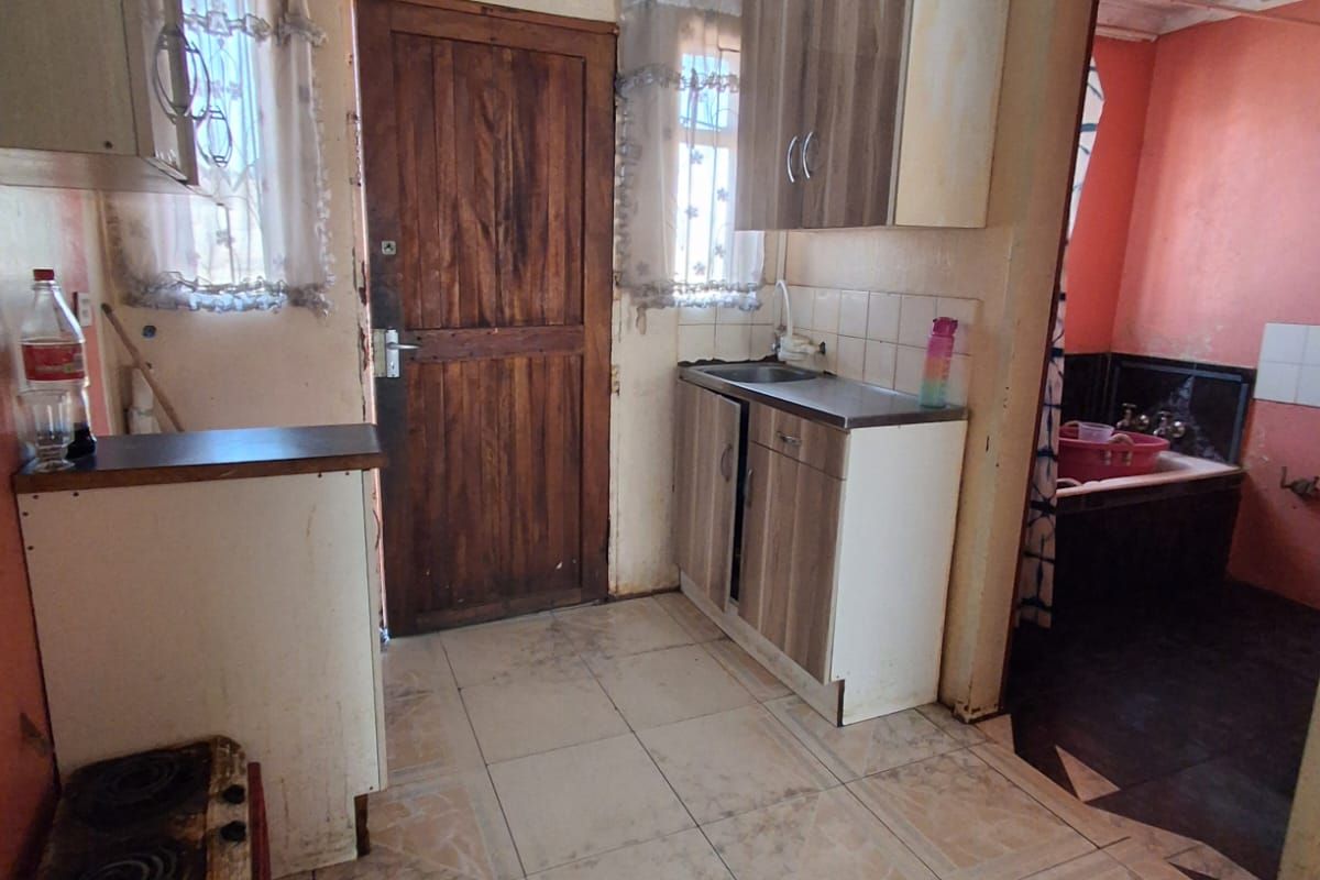 A compact kitchen featuring basic cabinetry, a sink, and tiled flooring, requiring significant cosmetic updates and repairs to the ceiling and wall finishes.