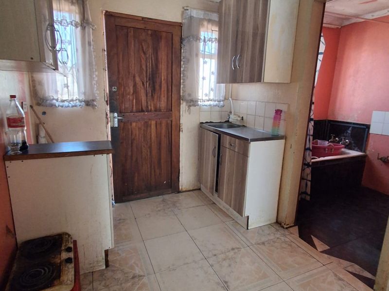 A compact kitchen featuring basic cabinetry, a sink, and tiled flooring, requiring significant cosmetic updates and repairs to the ceiling and wall finishes.