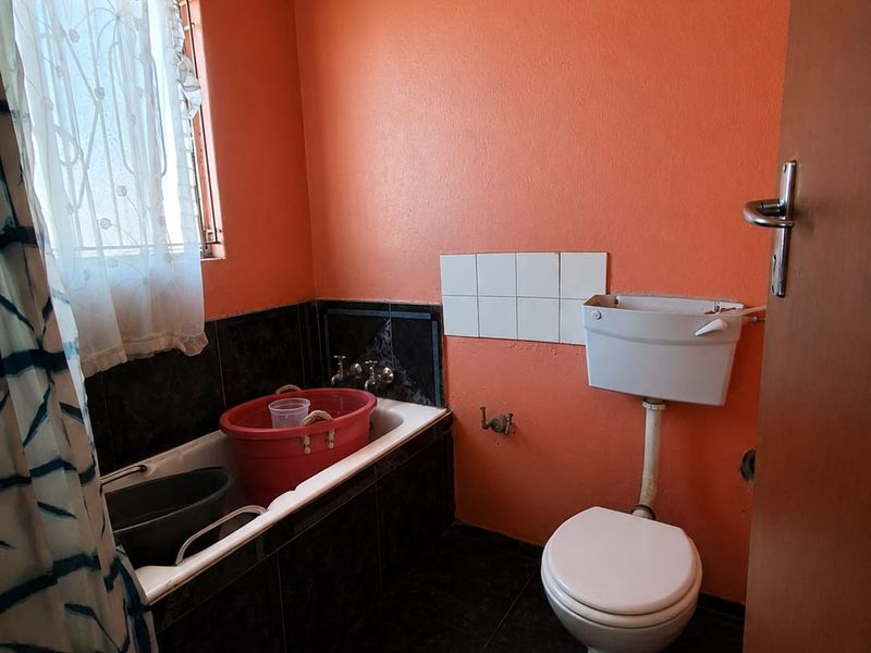 A dated bathroom featuring a bathtub, toilet, and dark tiled flooring, requiring cosmetic updates and modernization to improve its overall condition and appeal.
