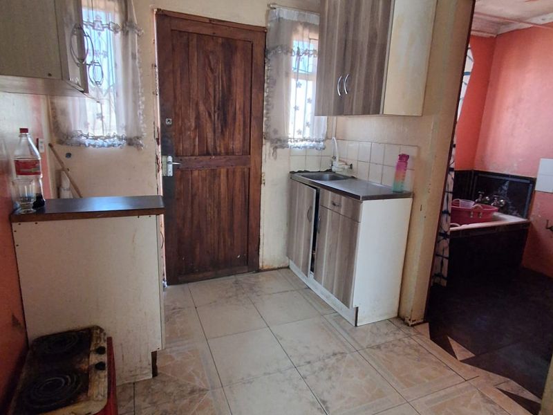 A compact kitchen area featuring tiled flooring, built-in cabinetry, and a stainless steel sink, requiring cosmetic updates and maintenance to improve its overall condition.