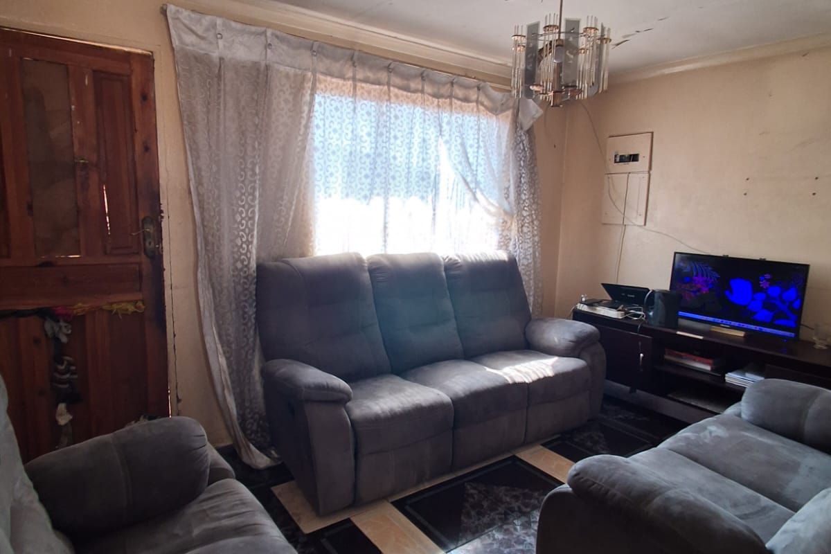 A living room featuring tiled flooring and a timber door, requiring cosmetic updates to the ceiling and wall finishes to improve the overall condition.