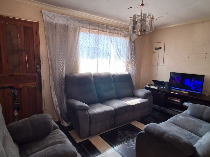 A living room featuring tiled flooring and a timber door, requiring cosmetic updates to the ceiling and wall finishes to improve the overall condition.
