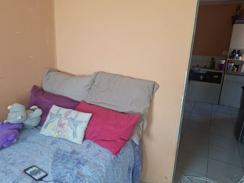 A bedroom with peach-toned walls and tiled flooring, featuring an open doorway leading into an adjacent kitchen area.
