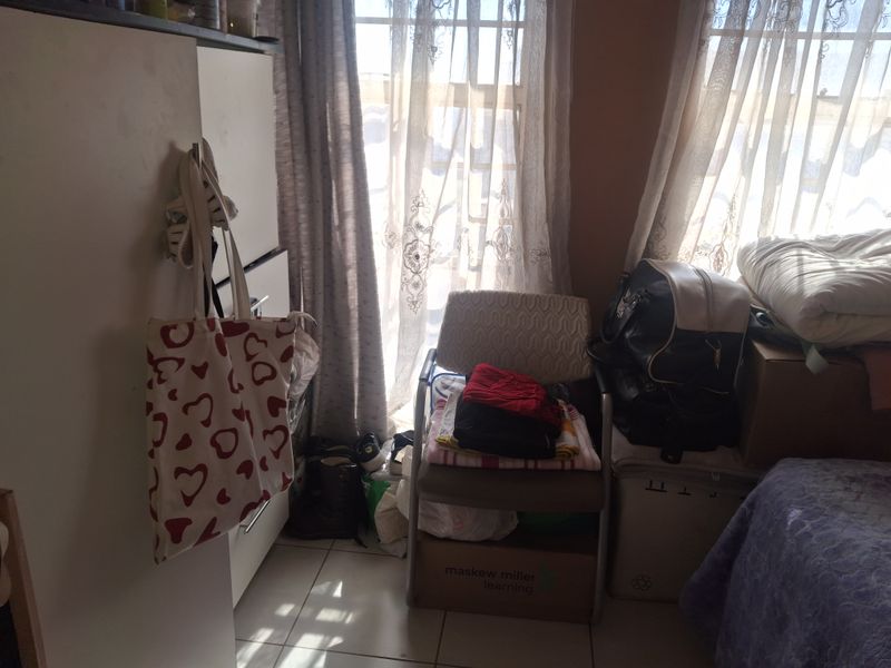 A bedroom featuring tiled flooring and a built-in cupboard, currently utilized with various personal items and storage.