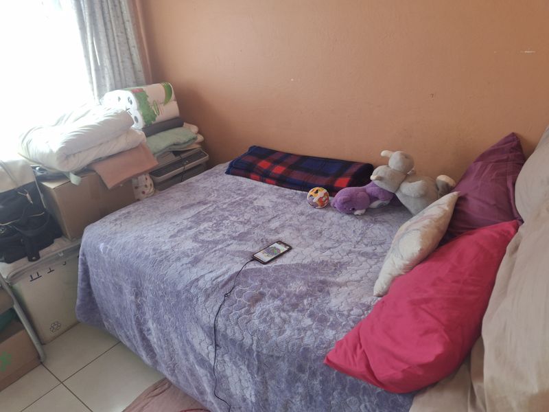 A compact bedroom featuring tiled flooring and plain wall finishes, offering a functional space that could benefit from cosmetic updates.