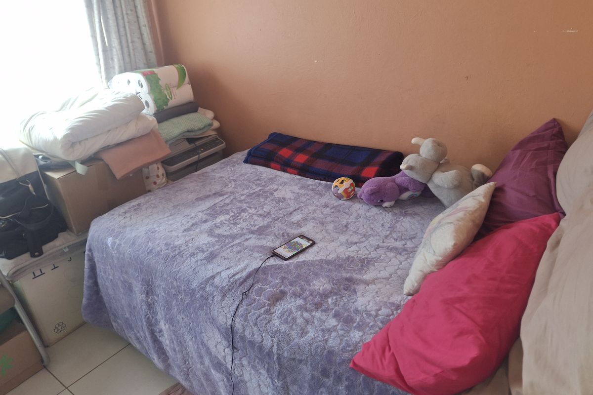 A compact bedroom featuring tiled flooring and plain wall finishes, offering a functional space that could benefit from cosmetic updates.
