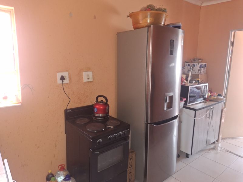A functional kitchen area featuring a freestanding electric stove, tiled flooring, and basic cabinetry, currently showing signs of wear on the wall surfaces.