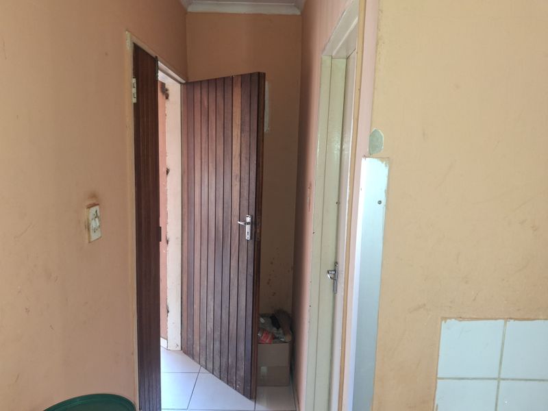 A narrow interior hallway featuring wooden doors and tiled flooring, currently showing signs of wear and requiring cosmetic updates to the wall finishes.