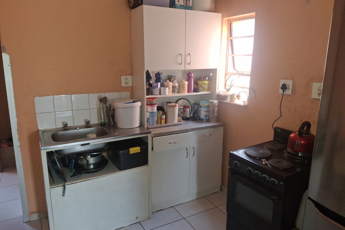 A compact kitchen featuring built-in cabinetry, a stainless steel sink, tiled splashback, and ceramic floor tiles, requiring cosmetic updates to improve its overall condition.