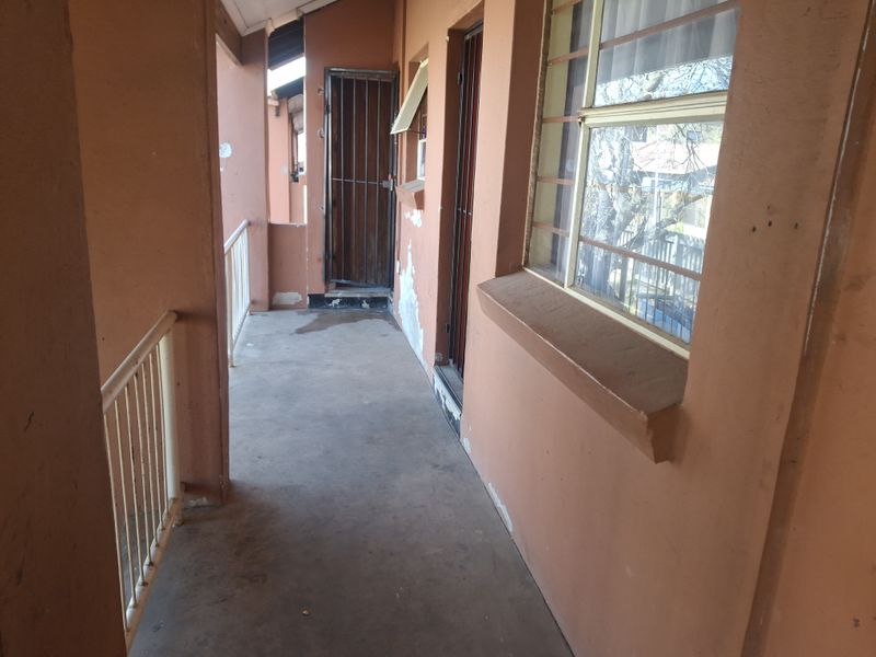 An exterior apartment balcony featuring a metal balustrade, security gates, and windows with security bars, showing signs of significant wear and peeling paint.