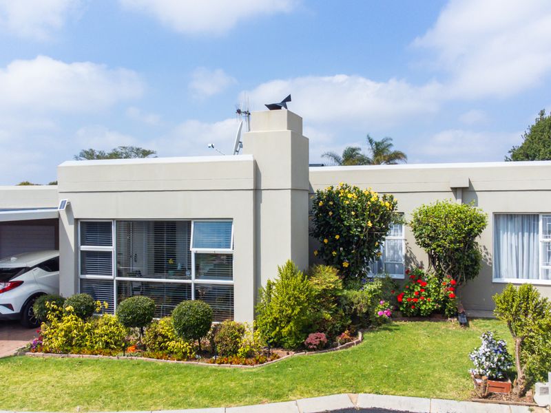 Front elevation of a townhouse featuring a paved carport, well-maintained garden, and a prominent chimney stack.