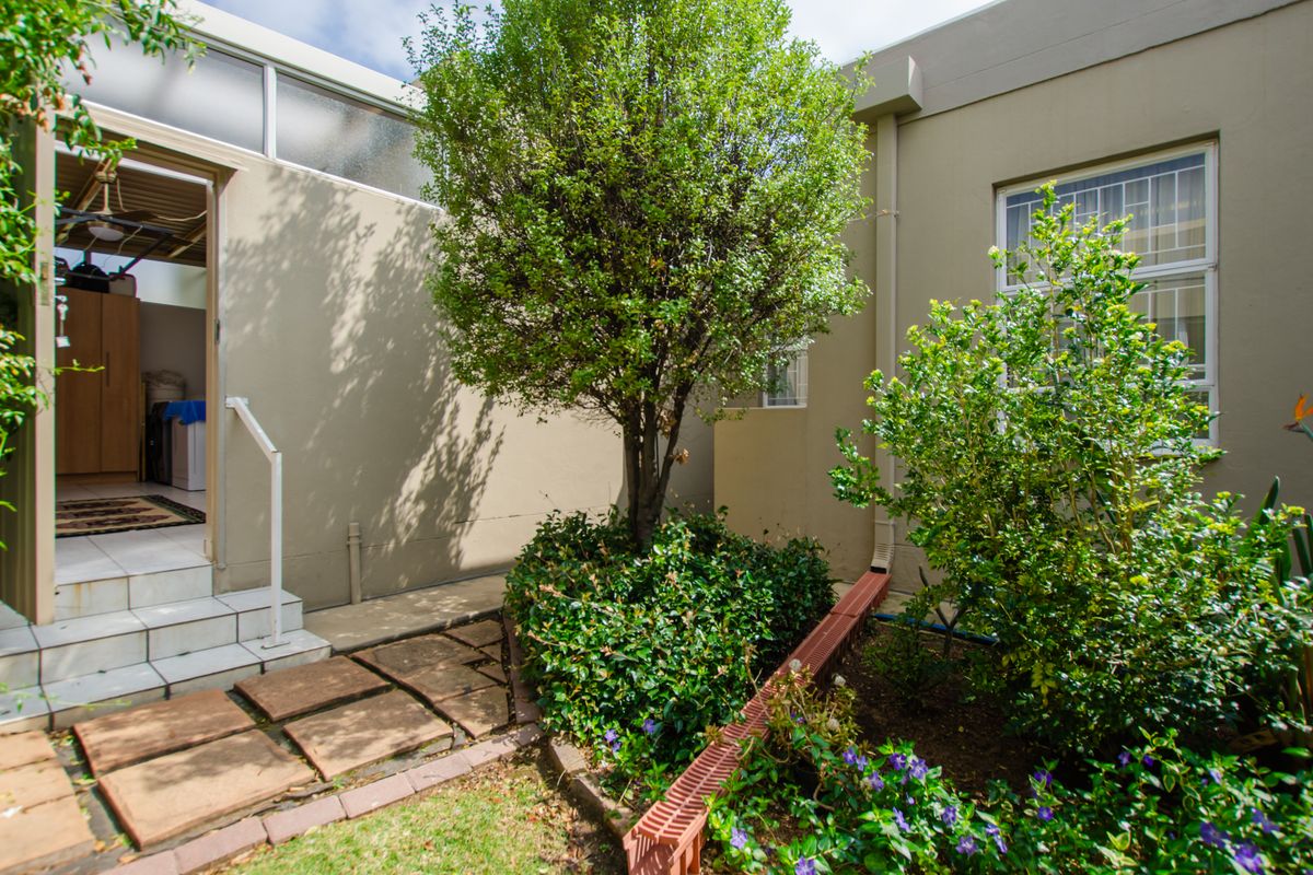 A private rear courtyard area featuring paved steps, established garden beds, and direct access to the interior living space.