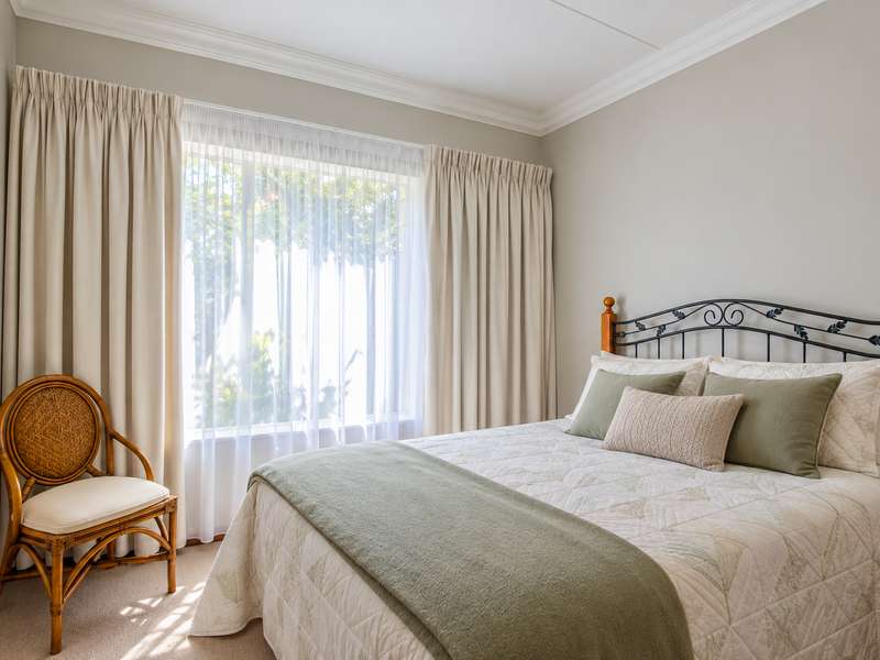 A well-maintained bedroom featuring neutral wall tones, crown molding, and carpet flooring, offering a bright and comfortable living space.