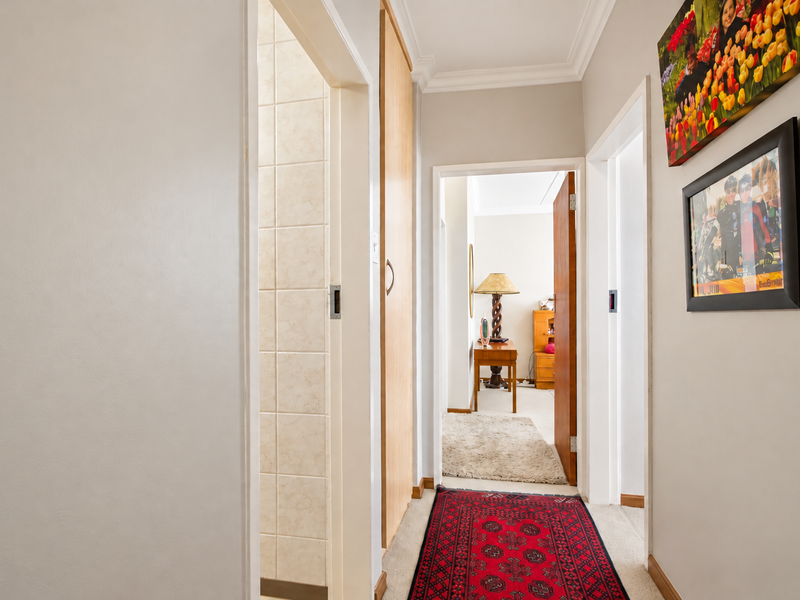 A well-maintained hallway featuring crown molding, neutral wall finishes, and access to adjacent rooms with built-in storage cabinetry.