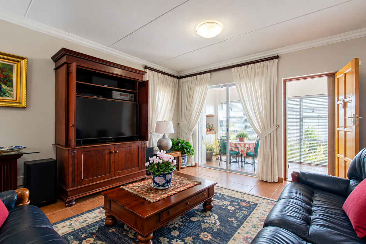 A comfortable living room featuring tiled flooring, coving, and a sliding glass door that provides access to an adjoining patio area.