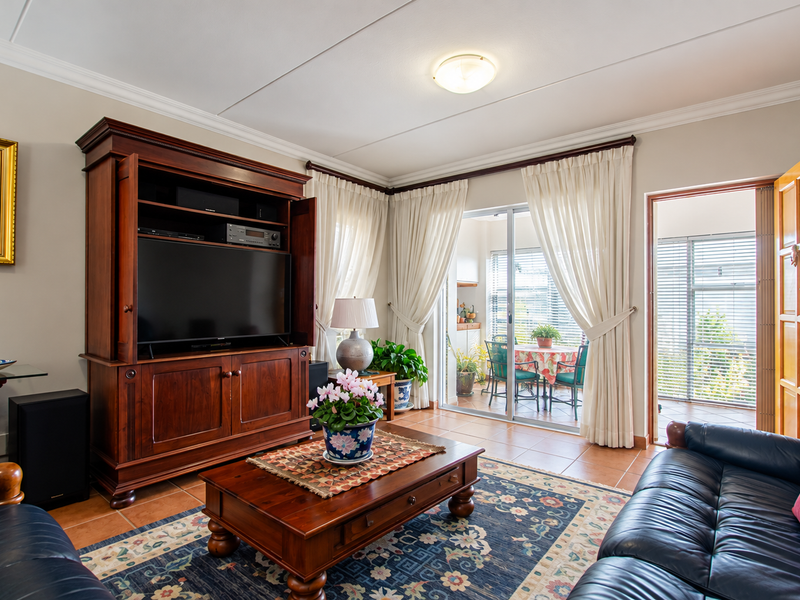 A comfortable living room featuring tiled flooring, coving, and a sliding glass door that provides access to an adjoining patio area.