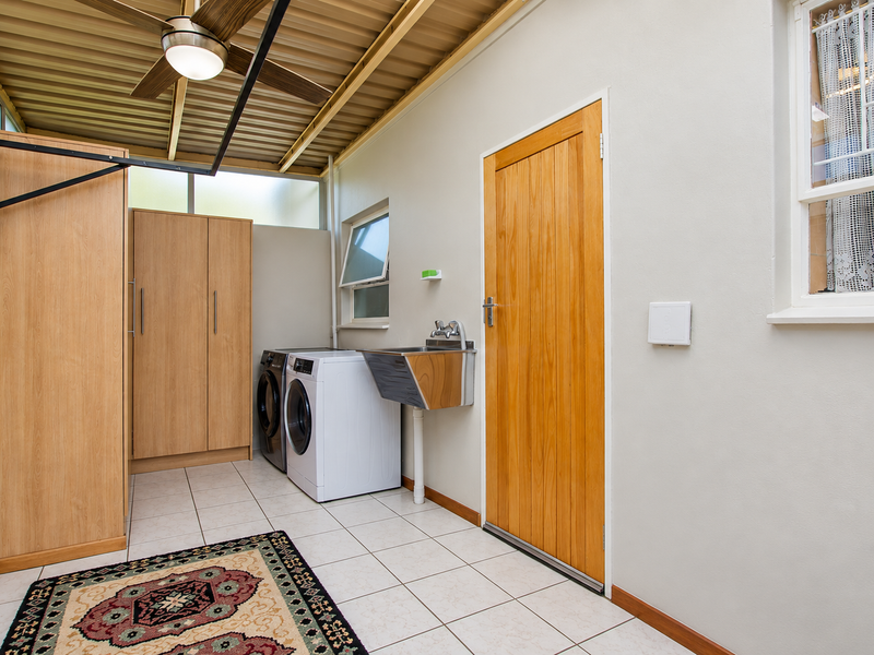 A clean and functional laundry room featuring built-in cabinetry, a stainless steel sink, tiled flooring, and a ceiling fan.